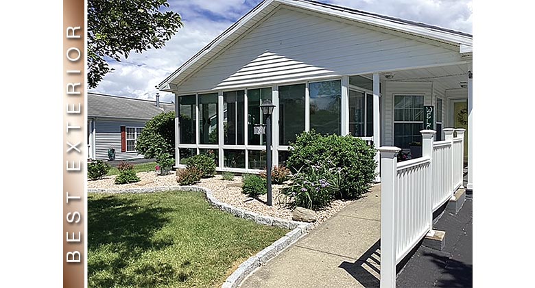 BEST EXTERIOR: White patio enclosure with glass knee wall, gable roof. Lamp post, neat plantings & fence in front.