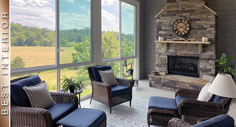 BEST INTERIOR: A nicely furnished sunroom with wicker chairs, fireplace and a view of a field and trees in the distance.