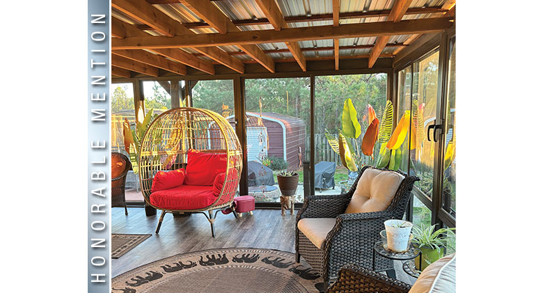 HONORABLE MENTION: Evening light highlighting the furnishings of brown sunroom with metal and wood roof, view of backyard.