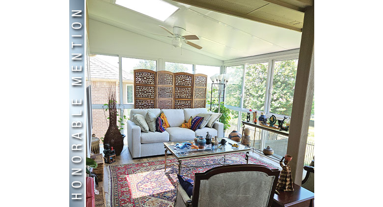 HONORABLE MENTION: Gray sofa w/pillows, oriental rug, glass coffee table in front of decorative screen in sunroom w/skylight.