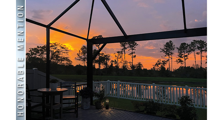 HONORABLE MENTION: Sunset viewed through screen enclosure with picture window and view of water and trees beyond.