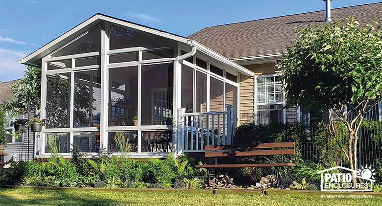 Screened room with shingled, gabled roof and lush plantings with park bench surrounding it.