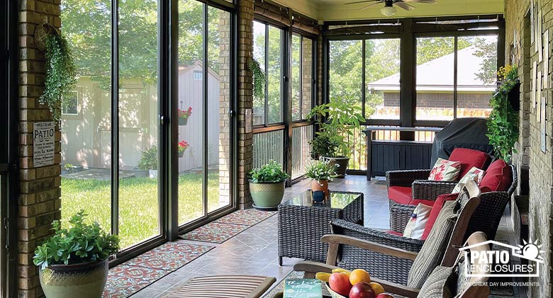 : Interior of a brown screen room with picket railing, tile floor, brown wicker furniture with red cushions.