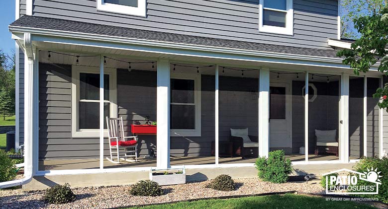 Exterior of a gray house with a long, screened-in porch across the back. White and red furniture inside the porch.