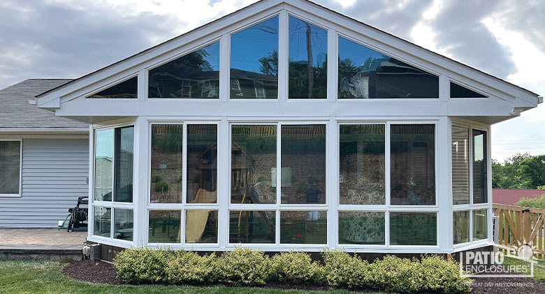 Large three-season room with gabled roof, glass wings and glass knee wall. A row of small bushes planted in front.