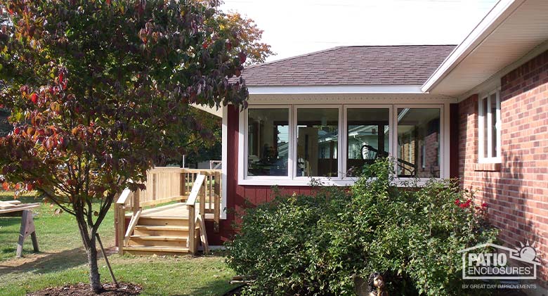 Traditional room addition with a wall of windows, dark red siding, and a shingled roof; small deck in front.