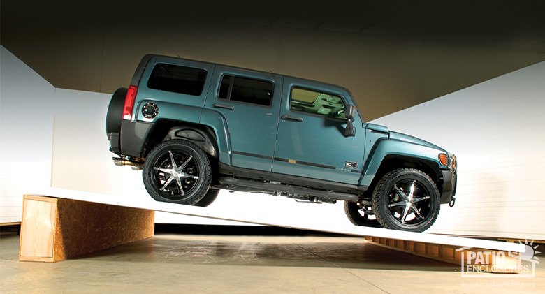 A blue hummer SUV parked on a piece of Patio Enclosures roofing that is lifted off the ground to show strength