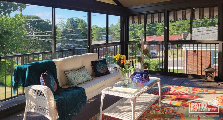 Screen porch enclosure with picket railing, white couch and coffee table, bright rug and throw pillows.