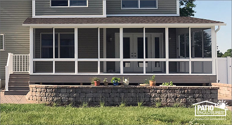 A screened porch enclosure on back of a home with a raised garden and paver patio. Small potted plants on garden wall.