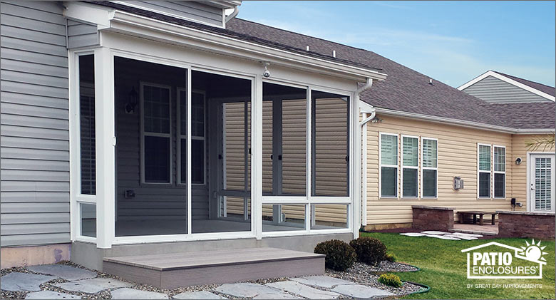 A corner screen enclosure on a gray house with sliding screen doors and one step down to a stone path.