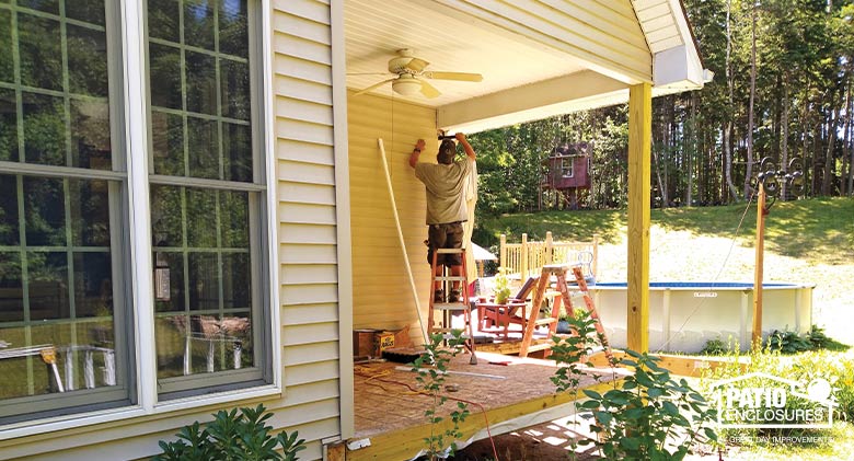 Photo of a workman on a ladder working on a corner porch on a tan home.