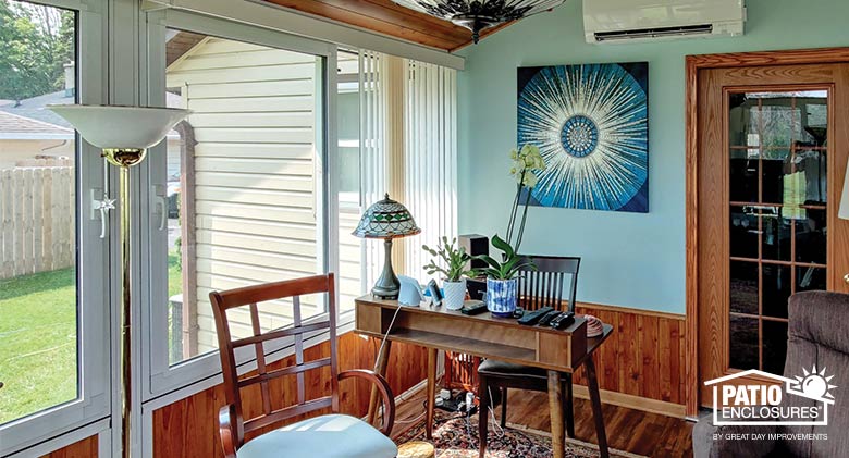 Small desk and chair in a sunroom home office with blue wall and wood paneled knee wall, abstract painting on wall.