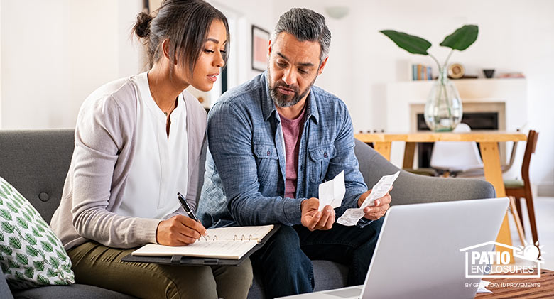 Couple sitting on a sofa looking at receipts and laptop computer; woman is poised to write notes in a notebook.