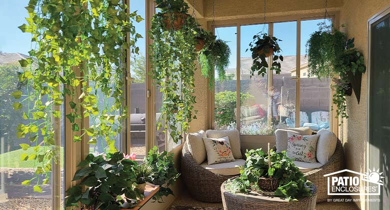 Tan sunroom with hanging and potted plants, two round chairs with floral pillows and round coffee table