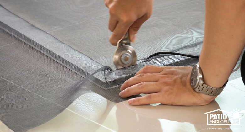 Photo of hands fixing a screen with rotary tool pushing spline into the frame.