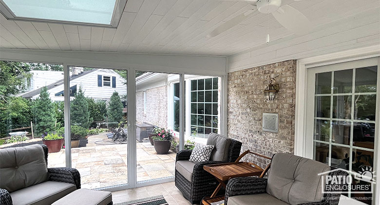 Sunroom patio enclosure with comfortable brown furniture, ceiling fan, and glass roof panel