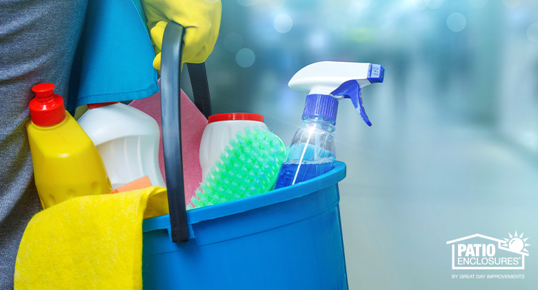 Hand in rubber glove holding a blue bucket of cleaning supplies, rags, and a brush