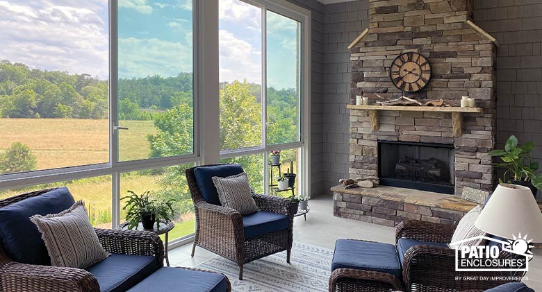 Interior of a sunroom with stone fireplace on the far wall and brown wicker furniture with dark blue cushions, tan pillows.