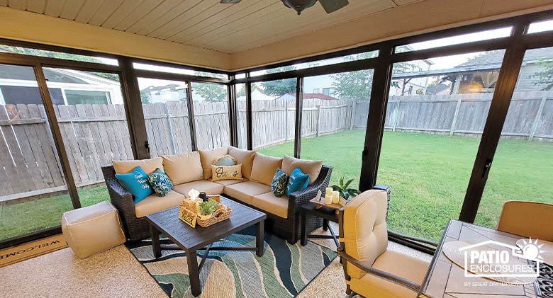 Patio enclosure has sofa with tan cushions, blue pillows, side table and coffee table. Dining table/chairs in foreground.” Table & chairs outside.