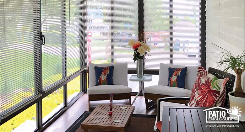 White mini blinds in a brown sunroom opened for an obscured look at the outdoors, modern furniture with bright accents..