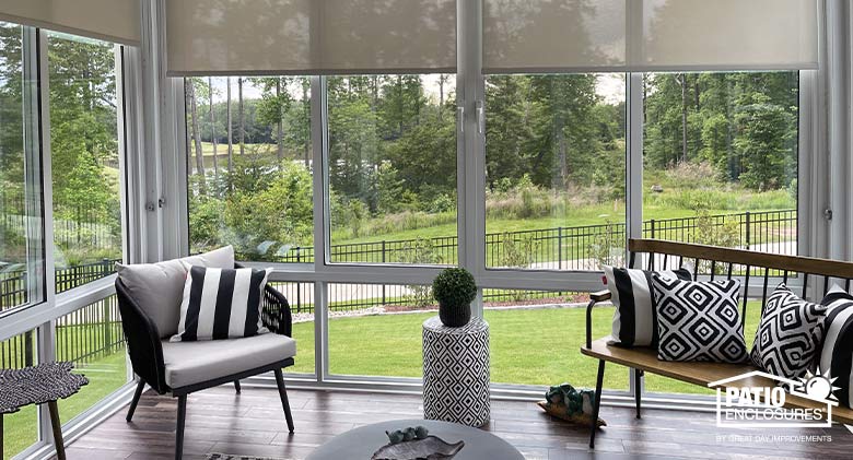 A white second-story sunroom with open shades on the windows and black and white furnishings.