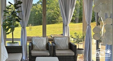 Interior of a tan sunroom with floor-to-ceiling tied back curtains and comfortable brown and beige furniture.