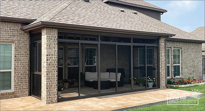 The exterior of a brown screened patio enclosure on a brown brick home furnished with a white sofa and potted plants.