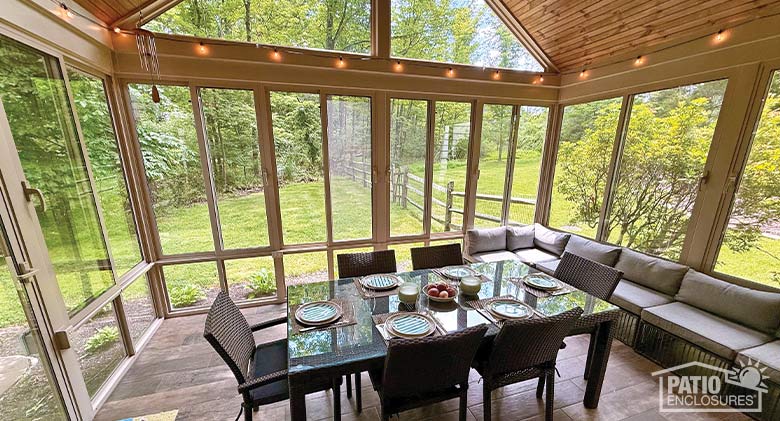 Sunroom Cost Photo Gallery The interio a glass sunroom with beige frame and furnished with a long sofa and a dining table and chairs in the center.