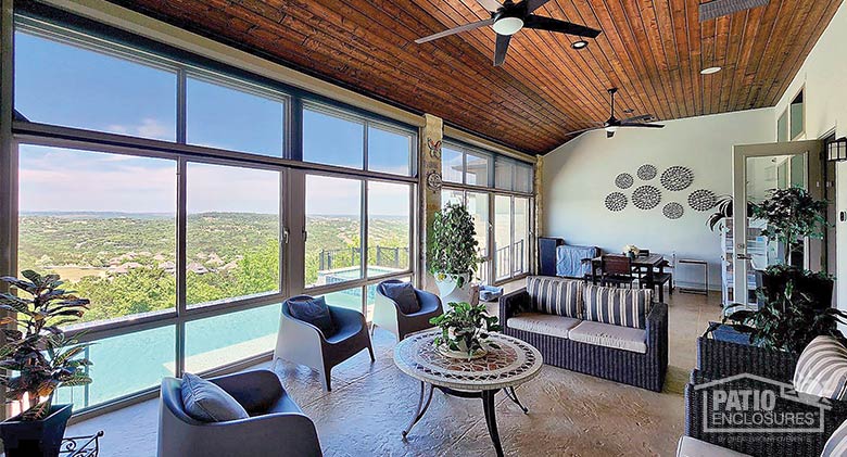 Interior of a sunroom with a comfortable seating area and a dining table and chairs and a view of pool and landscape.