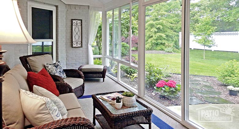 Tan furniture in the interior of a patio enclosure with seating that maximizes views of the backyard lawn and plantings.