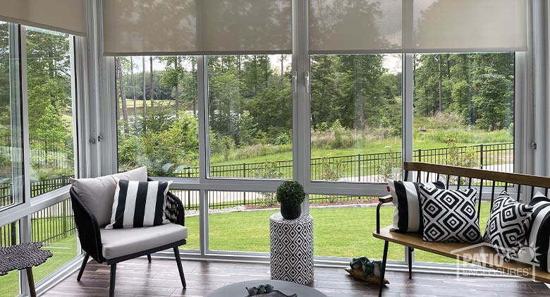 Modern furniture with black and white geometric pillows in a white Florida room with roller shades and wood floor.