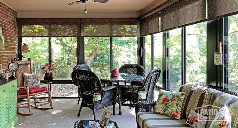 Brown wicker table and chairs, rocking chair, and a wicker loveseat with striped cushions in a brown glass sunroom.