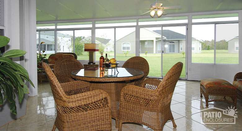 The interior of a white sunroom with solid knee wall, beige tiled floor, and wicker dining table and chairs.