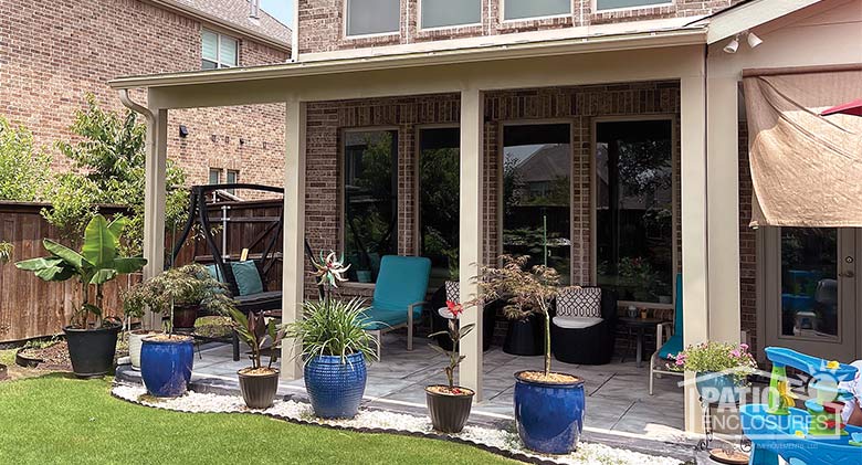 A patio covered with a beige roof with four posts and alternating blue and black pots lined up in front of it.