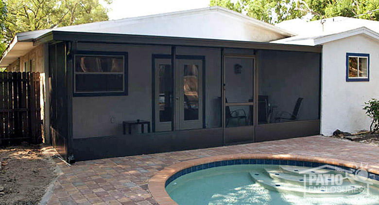 A portion of an in-ground pool is visible in front of a brown screen room lanai enclosure with kickplate and screen door.