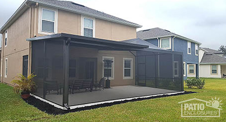 A white lanai enclosure with solid roof, screen door, and kickplate on a tan stucco home.
