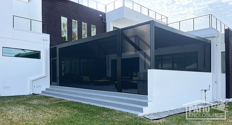 Exterior of a brown screen room with picture windows built on white concrete patio on a modern home.