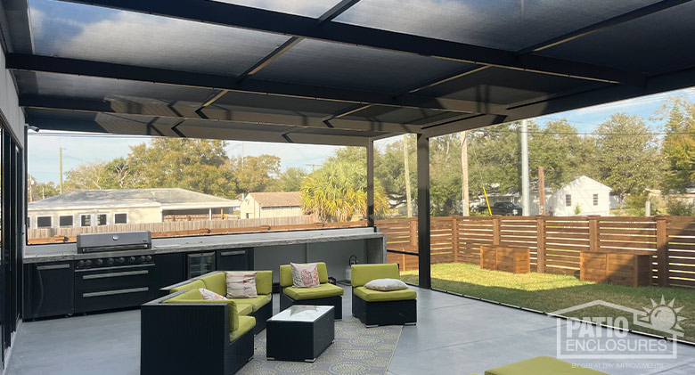 View from the interior of a brown screen room with picture windows, comfortable furniture, and an outdoor kitchen.