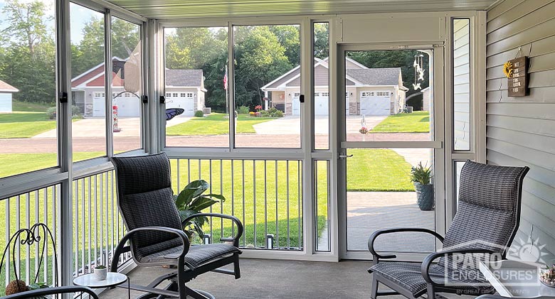 View of homes across the street from the corner of a white screen room with picket railing and two chairs inside.