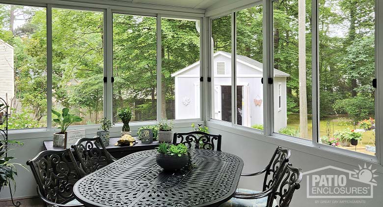 The interior of a white screen room with solid knee walls furnished with wrought iron table and chairs.