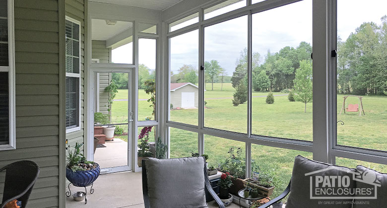 Looking at a backyard landscape with shed, wooden swing, bushes, and trees from the interior of a screen room.