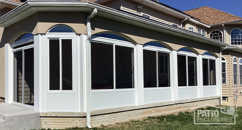 A covered patio with scalloped edges enclosed with a white screen room with solid knee walls and sliding doors on the end.