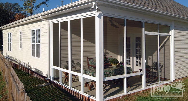 A corner screen room in white with a covered table and chairs inside the room.