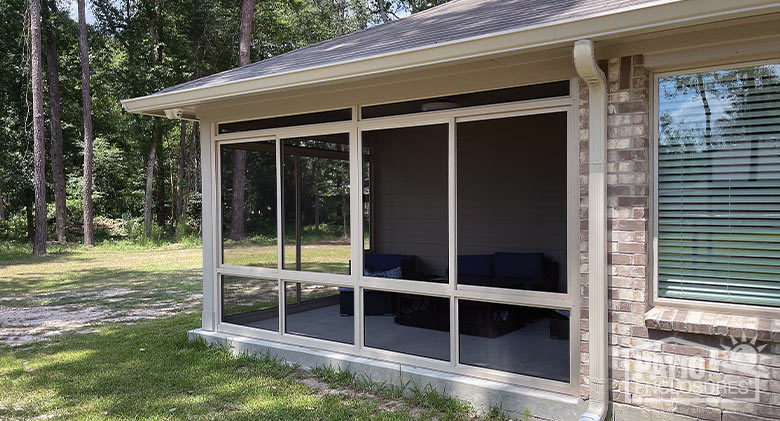 Beige screen room enclosing a corner patio with a cushioned chair and loveseat inside.