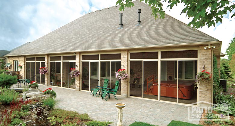 A large screen room patio enclosure on a brick building with hanging flower baskets outside and garden in the foreground.