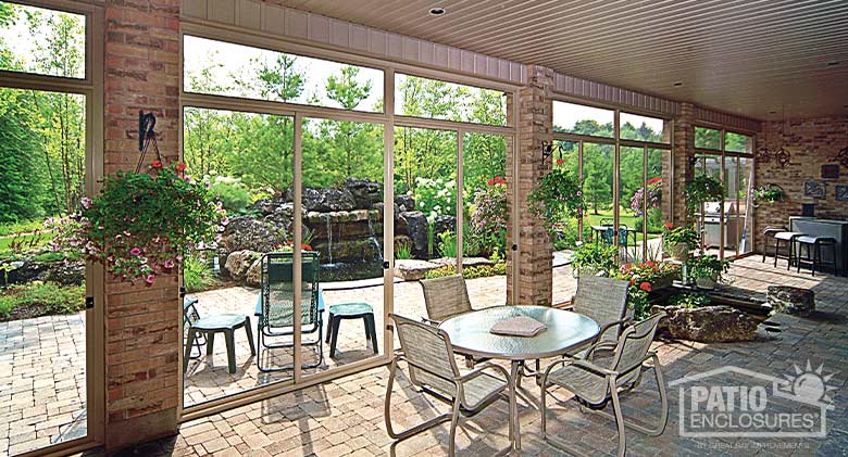 Table, chairs, and hanging flowers inside a screen room patio enclosure. View of gardens and a water feature outside.