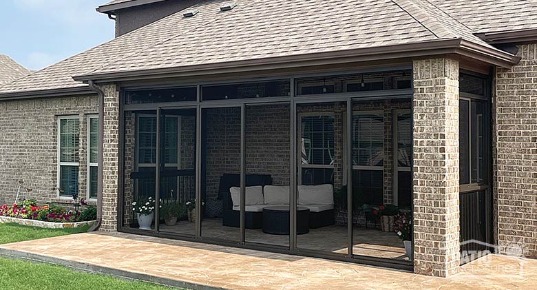 A covered lanai or porch enclosed by a dark brown screen room and containing comfortable seating and potted flowers.