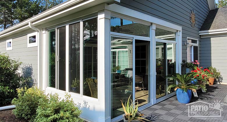 A white framed glass-enclosed lanai or porch with potted plants and flowers outside.