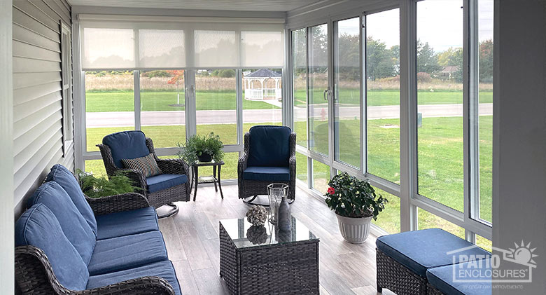 Brown wicker furniture with dark blue cushions inside a glass-enclosed lanai accented with potted plants.