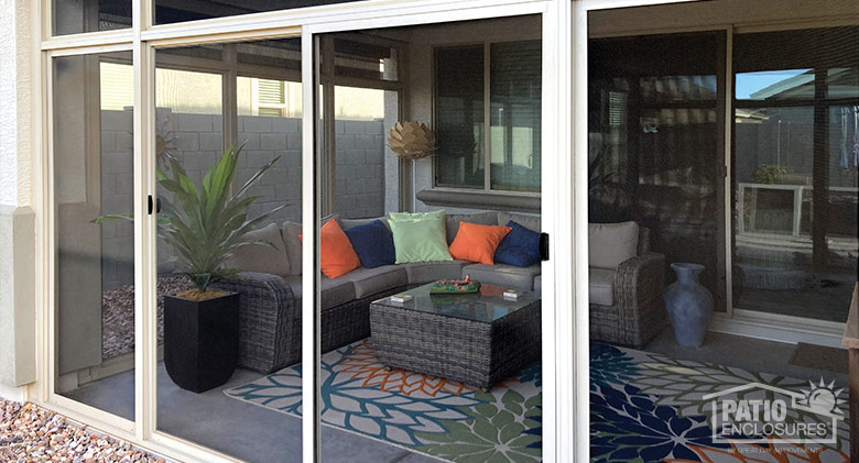 View into a screen lanai enclosure decorated with a wicker couch, brightly colored pillows, a coffee table, and potted plant.